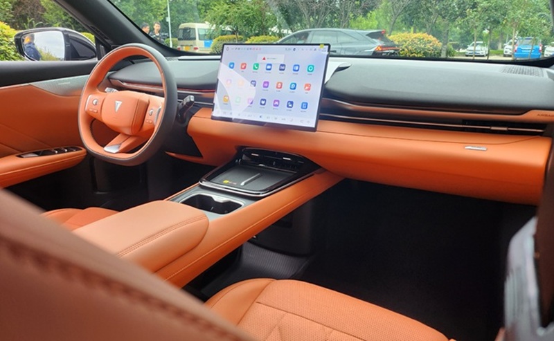 Orange leather car interior with a large tablet-style touchscreen display mounted on the dashboard showing app icons and maps.